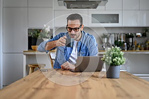 Portrait of smiling handsome man drinking coffee and working over laptop on desk at home office
