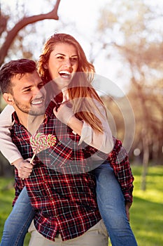 Portrait of smiling handsome man giving piggy back to his girlfriend in the nature