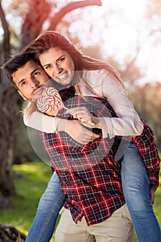 Portrait of smiling handsome man giving piggy back to his girlfriend in the nature