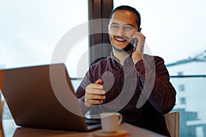 Portrait of smiling handsome man working at laptop, talking on smartphone, background of panoramic windows