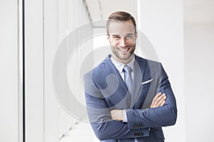 Portrait of smiling handsome young businessman standing with arms crossed in new office