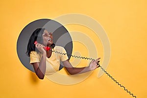 Portrait of a smiling happy afro american woman in sunglasses talking on retro telephone in a round hole circle in yellow