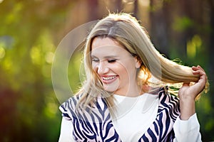 Portrait of smiling happy beautiful blonde 30 years old woman touching hair and laughing with closed eyes in forest. Freedom,