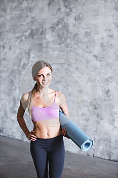 Portrait of a smiling happy charming fitness girl with yoga mat