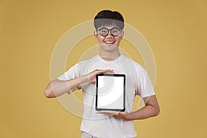 Portrait of smiling happy cheerful young asian man dressed casually showing blank digital tablet screen isolated on yellow