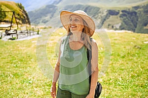 Portrait of a smiling happy elderly woman tourist traveling with a camera posing against backdrop of mountains. Old