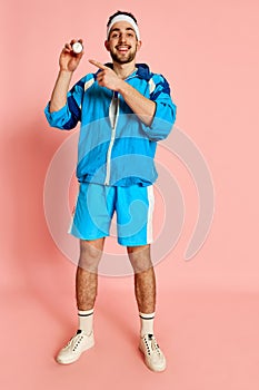 Portrait of smiling happy fitness trainer, coach in blue uniform posing with whistle and taimer against pink studio