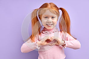 portrait smiling happy little girl making heart sign with hands isolated on purple background.