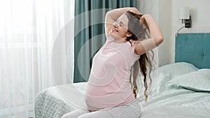 Portrait of smiling happy pregnant woman in pajamas stretching on bed at morning after waking up. Concept of happiness