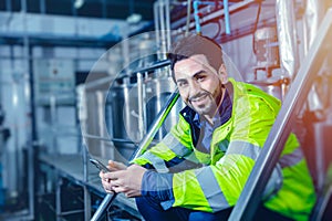 Portrait smiling happy smart latin engineer worker sitting relax in plant industry factory hand holding smartphone blue colortone