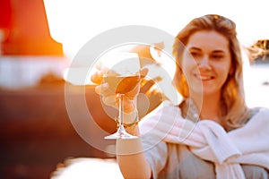 Portrait of smiling happy woman with long wavy fair hair, wearing white sweater, grey shirt, standing on embankment.