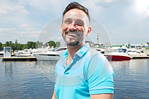 Portrait of smiling happy yachtsman on marina with boat background. Summer vacation yachting time for male lifestyle