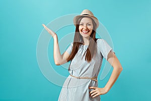 Portrait of smiling happy young elegant woman wearing dress, straw summer hat pointing hand aside on copy space isolated