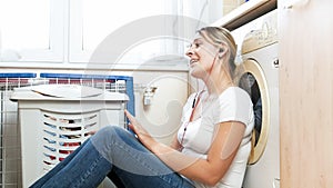 Portrait of smiling young housewife singing and listening to music at laundry room