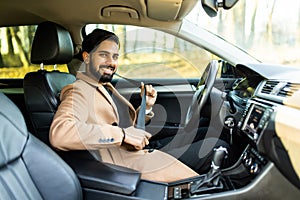 Portrait of smiling indian man fastening seat belt and sitting in his car