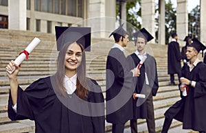 Portrait of smiling joyful girl student in a university graduate gown and diploma in her hands.