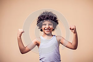 A portrait of smiling kid boy with curly hair showing strong. Children and health concept