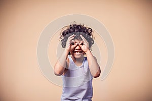 A portrait of smiling kid boy showing binocular gesture. Children and emotions concept