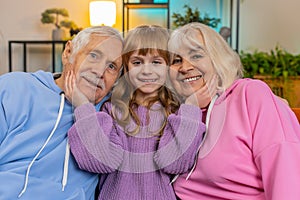 Portrait of smiling kid granddaughter and loving grandfather and grandmother looking at camera home