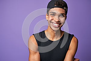 Portrait of smiling latino transgender man in black t-shirt and cap on purple background