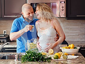 Portrait of smiling laughing white Caucasian couple two people pregnant woman with husband cooking food, drinking citrus juice