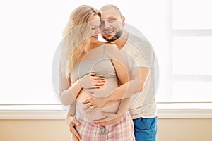 Portrait of smiling laughing white Caucasian young middle age couple, pregnant woman with husband in room hugging cuddling
