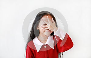 Portrait of smiling little Asian child girl in scarlet red dress covering eyes with hand isolated over white background