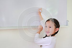 Portrait of Smiling little Asian child girl or Schoolgirl writing something on whiteboard with a marker and looking up in the