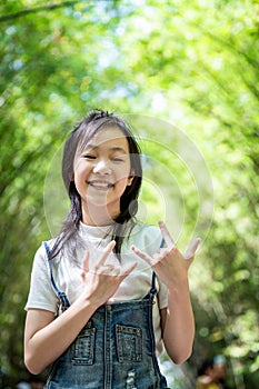 Portrait of smiling little asian girl right sign language meaning I Love You and look at the camera on bamboo forest,green nature