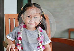 Portrait of smiling little asian girl with welcome orchids flower garland sitting on the chair