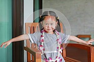 Portrait of smiling little asian girl with welcome orchids flower garland sitting on the chair