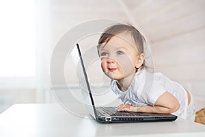 Portrait of smiling little baby girl with a laptop at home