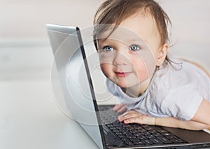 Portrait of smiling little baby girl near a laptop on a table