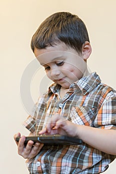 Portrait of a smiling little boy holding mobile phone isolated over light background. cute kid playing games on smartphone.