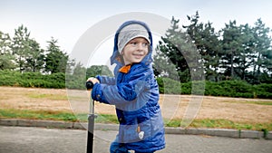 Portrait of smiling little boy in jacket riding on scooter in park