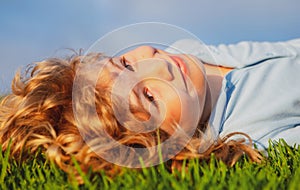 Portrait of a smiling little boy lying on green grass and dreaming. Cute child enjoying nature outdoors. Healthy