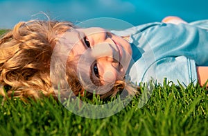Portrait of a smiling little boy lying on green grass and dreaming. Cute child enjoying nature outdoors. Healthy