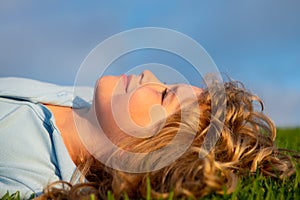 Portrait of a smiling little boy lying on green grass. Happy children relax on green grass in spring park. Healthy