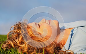 Portrait of a smiling little boy lying on green grass. Happy children relax on green grass in spring park. Healthy