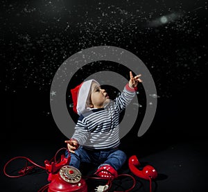 Portrait of smiling little boy wearing christmas hat near red vintage telephone sitting on black background