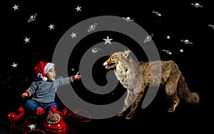 Portrait of smiling little boy wearing christmas hat sitting near vintage red telephone petting a fox on black background