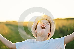 Portrait of a smiling little boy in a white T-shirt and hat playing outdoors on the field at sunset