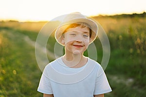 Portrait of a smiling little boy in a white T-shirt and hat playing outdoors on the field at sunset