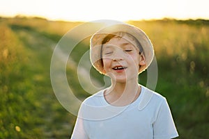 Portrait of a smiling little boy in a white T-shirt and hat playing outdoors on the field at sunset