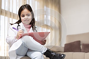 Portrait of smiling little child dressed in doctor`s uniform handwriting a report