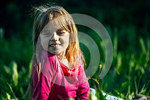 Portrait of a smiling little cute girl lying on green green grass.