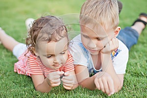 Portrait of a smiling little girl and boy lying on green grass