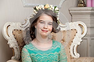 Portrait of a smiling little girl in the flower wreath sitting o