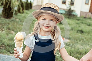 portrait of smiling little girl in straw hat with ice cream in hand looking