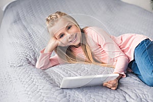 portrait of smiling little girl with tablet resting on bed